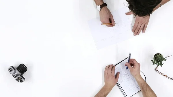 Top View Of Two People Discussing Notes And Using A Camera. (Thumbnail)