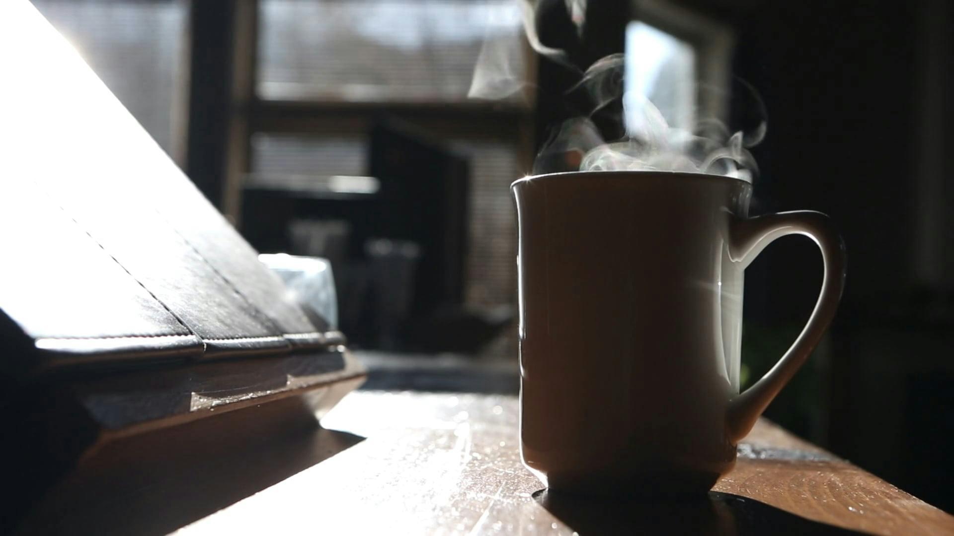 A Steaming Coffee Cup In A Cozy, Sunlit Interior Setting.
