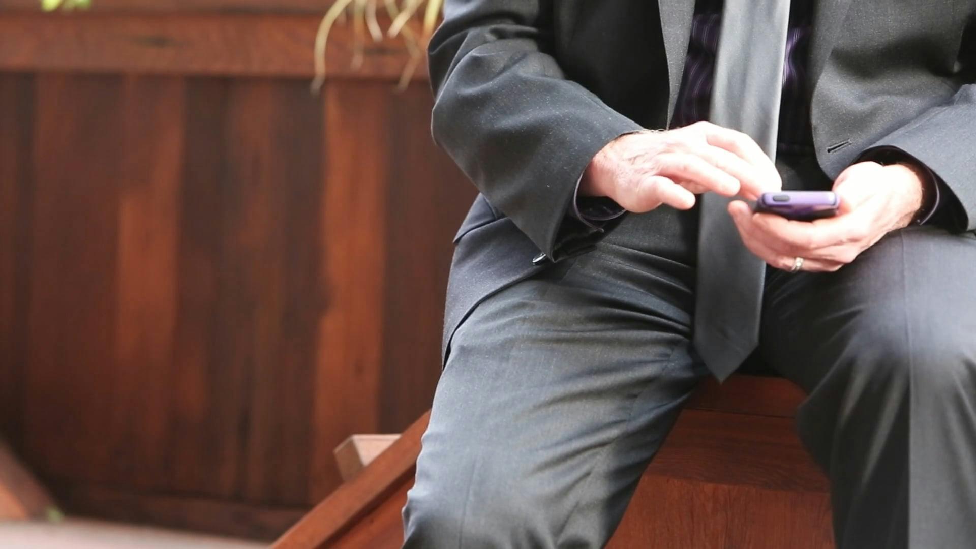 Businessman In Suit Texting On Smartphone While Seated On Wooden Steps.