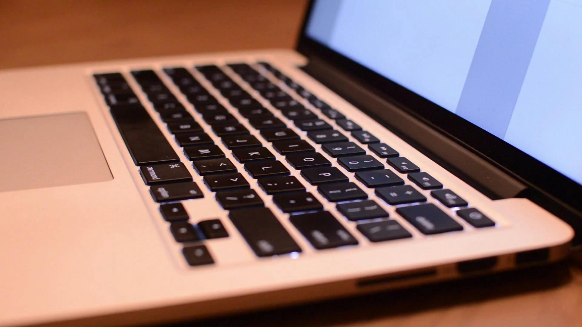 Hands Typing On A Laptop Keyboard In A Low-Light Setting.