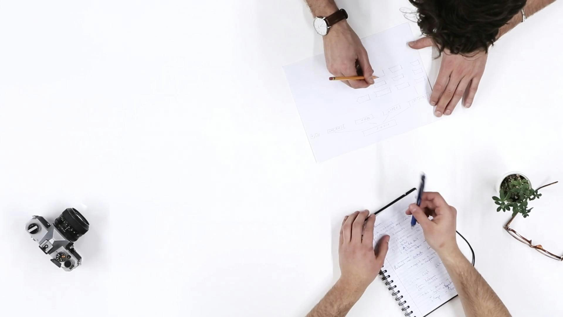 Top View Of Two People Discussing Notes And Using A Camera.