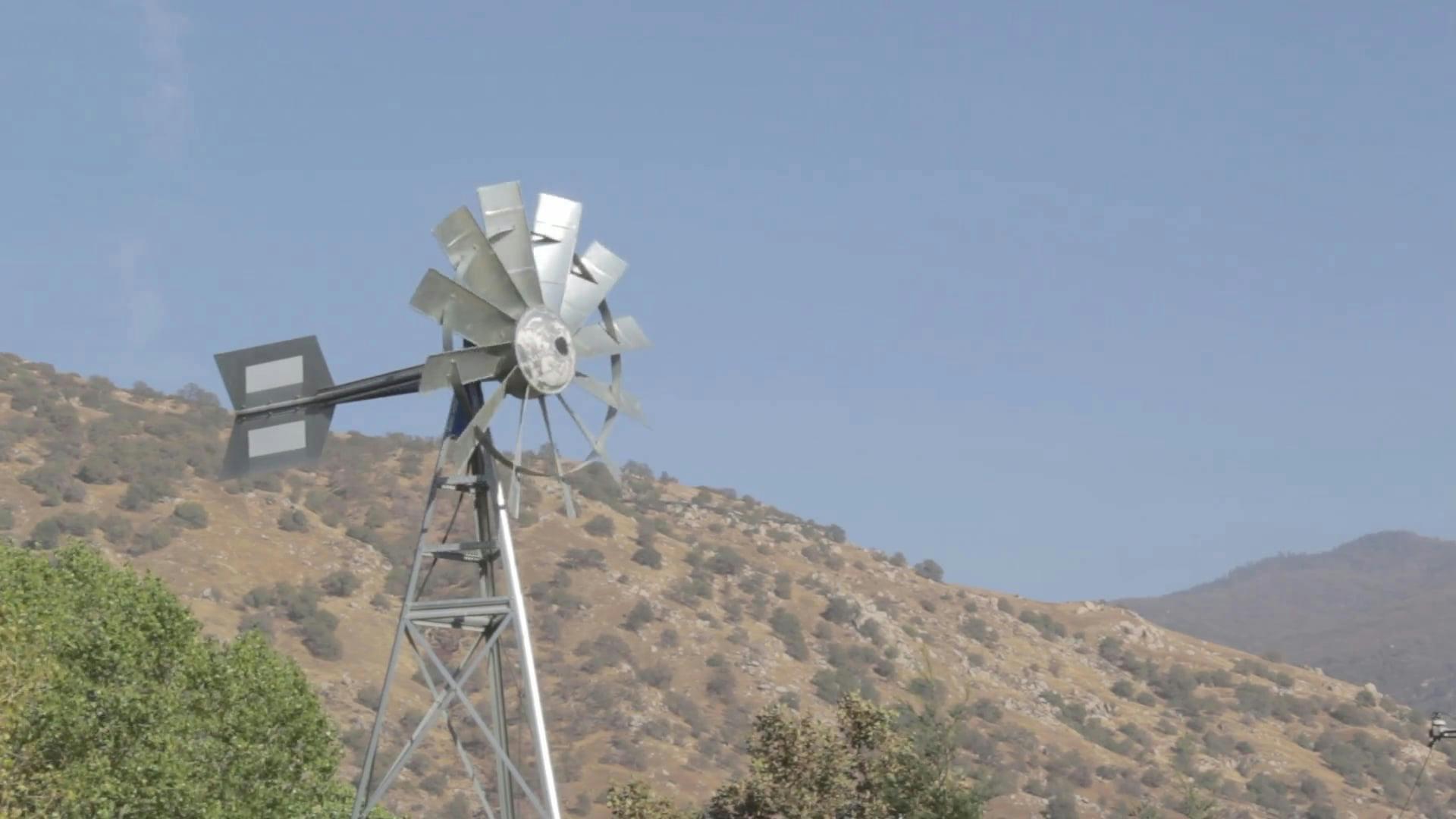 Windmill Spinning In A Mountainous Rural Landscape On A Clear Day.